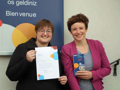 Lena Engesser, Leiterin der VHS-Ortenau (rechts), und Gewinnerin Monika Reinbold bei der Übergabe des Gutscheins vor der Geschäftsstelle Acher-Renchtal
