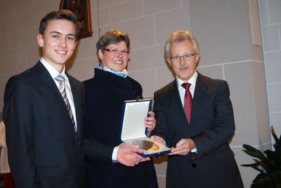 Bildunterschrift (v.r.n.l.): Dezernent Georg Benz (r.) überreichte die Zelterplakette an die Vorstandssprecherin Brigitte Kolbe, links Chorleiter Simon Meder. Foto: Karl Joggerst